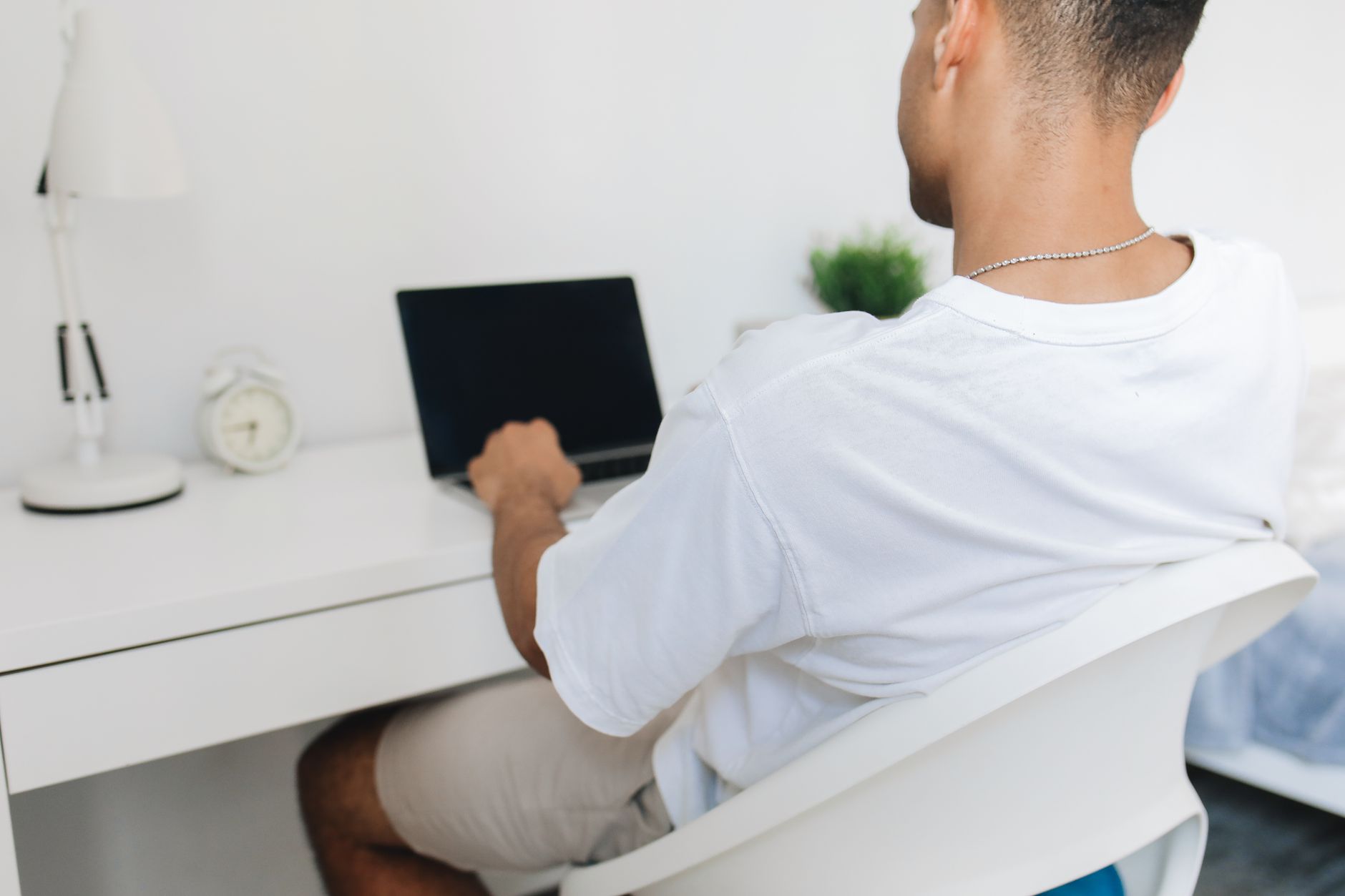 Man working on a laptop in a home study setting, focused from behind.